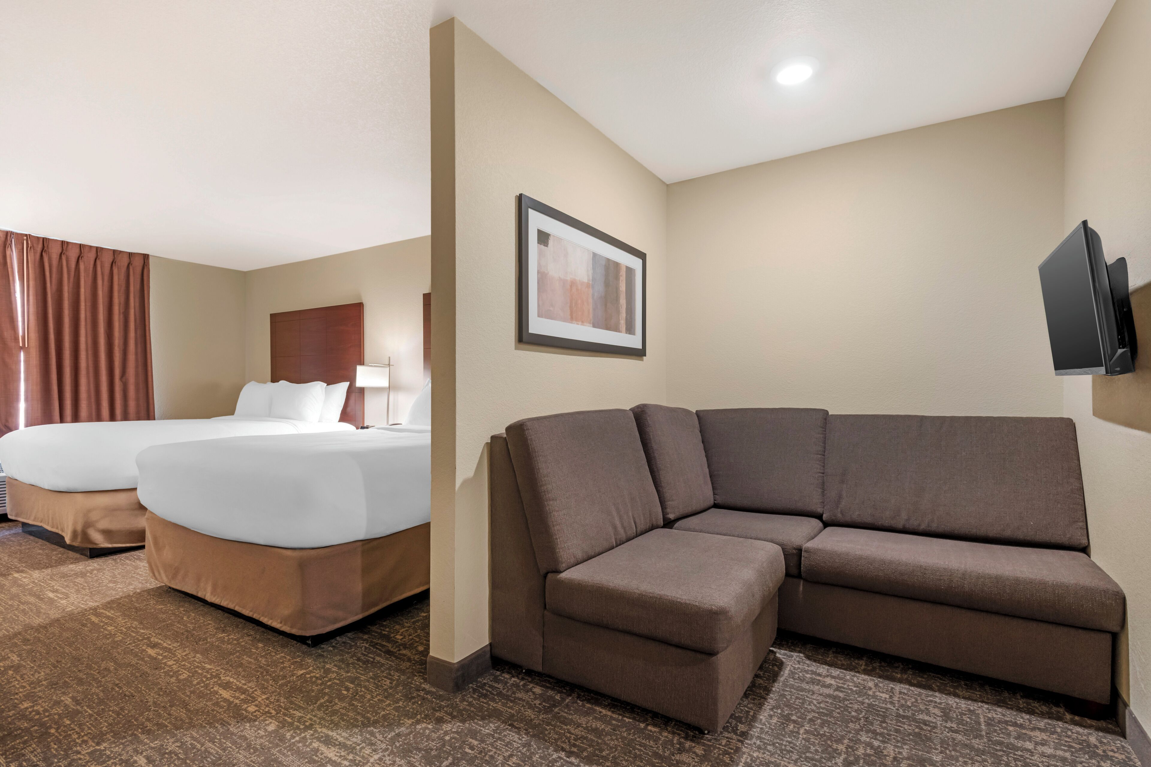 A hotel room with two beds, a sofa, a flat-screen TV, and a framed picture on the wall.