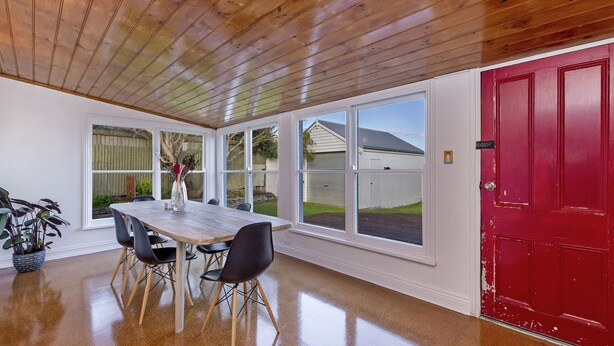 Un comedor con mesa y sillas de madera, ventanas amplias y una puerta roja.