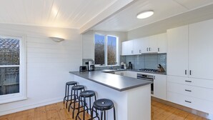 Una cocina moderna con armarios blancos, una isla central con taburetes, horno integrado y ventana que proporciona luz natural.