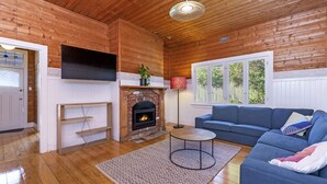 Una sala de estar acogedora con paredes de madera, una chimenea, un sofá azul y un televisor de pantalla plana sobre la chimenea.