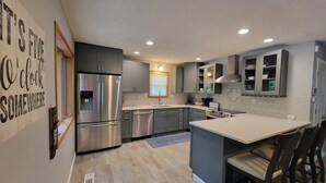 A modern kitchen with stainless steel appliances, grey cabinetry, and a central island with seating. - COZY 5 BEDROOM 3 BATH IN COVE WITH DOCK. SLEEPS 12. BASEMENT REMODEL MAY 2025. (Lake Ozark)