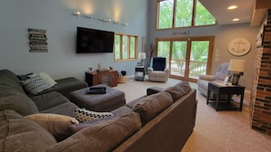 A spacious living room with a large window, a flat-screen TV, and a cozy seating area with a fireplace. - COZY 5 BEDROOM 3 BATH IN COVE WITH DOCK. SLEEPS 12. BASEMENT REMODEL MAY 2025. (Lake Ozark)
