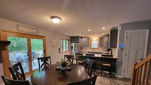 A modern kitchen with grey cabinets, a wooden dining table with chairs, and a view of the outdoors through a glass door. - COZY 5 BEDROOM 3 BATH IN COVE WITH DOCK. SLEEPS 12. BASEMENT REMODEL MAY 2025. (Lake Ozark)