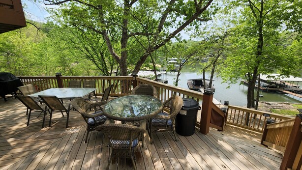 A wooden deck with outdoor furniture, overlooking a lake with boats. - COZY 5 BEDROOM 3 BATH IN COVE WITH DOCK. SLEEPS 12. BASEMENT REMODEL MAY 2025. (Lake Ozark)