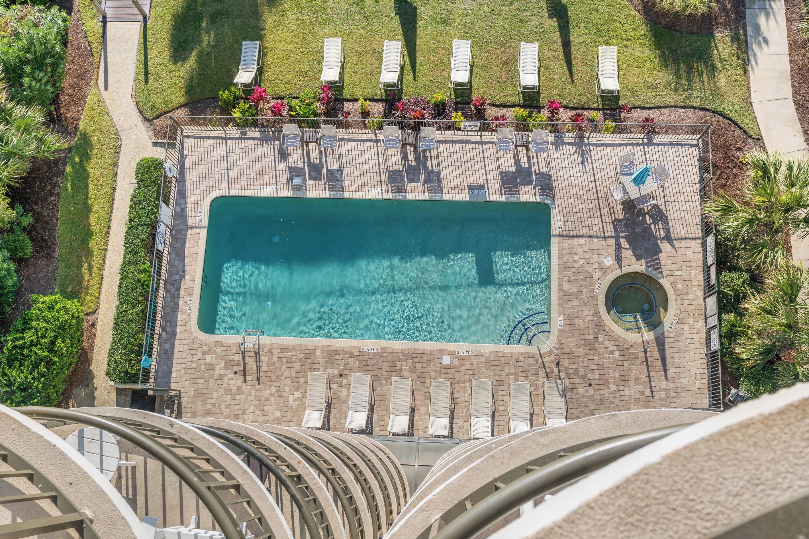 An aerial view of a swimming pool area with lounge chairs, a circular hot tub, and surrounding greenery.