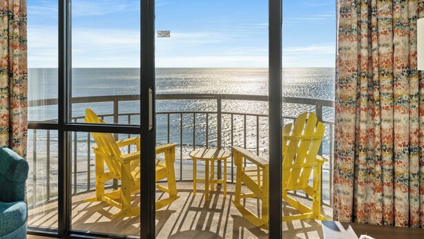 A balcony with a view of the ocean, yellow Adirondack chairs, and a table. - 10th Floor 1br Oceanfront w/ Spectacular Views! (Myrtle Beach)