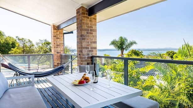 Een balkon met een witte tafel, een hangmat en uitzicht op zee.