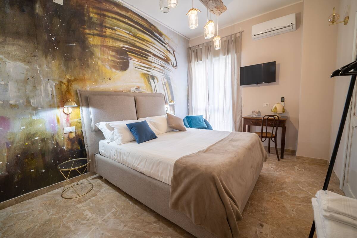 Un dormitorio con una cama grande, un escritorio, una silla, un televisor y una pared con un diseño abstracto original.