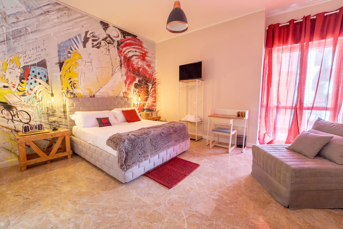 Un dormitorio moderno con una cama grande, un escritorio, un sofá y un mural en la pared.