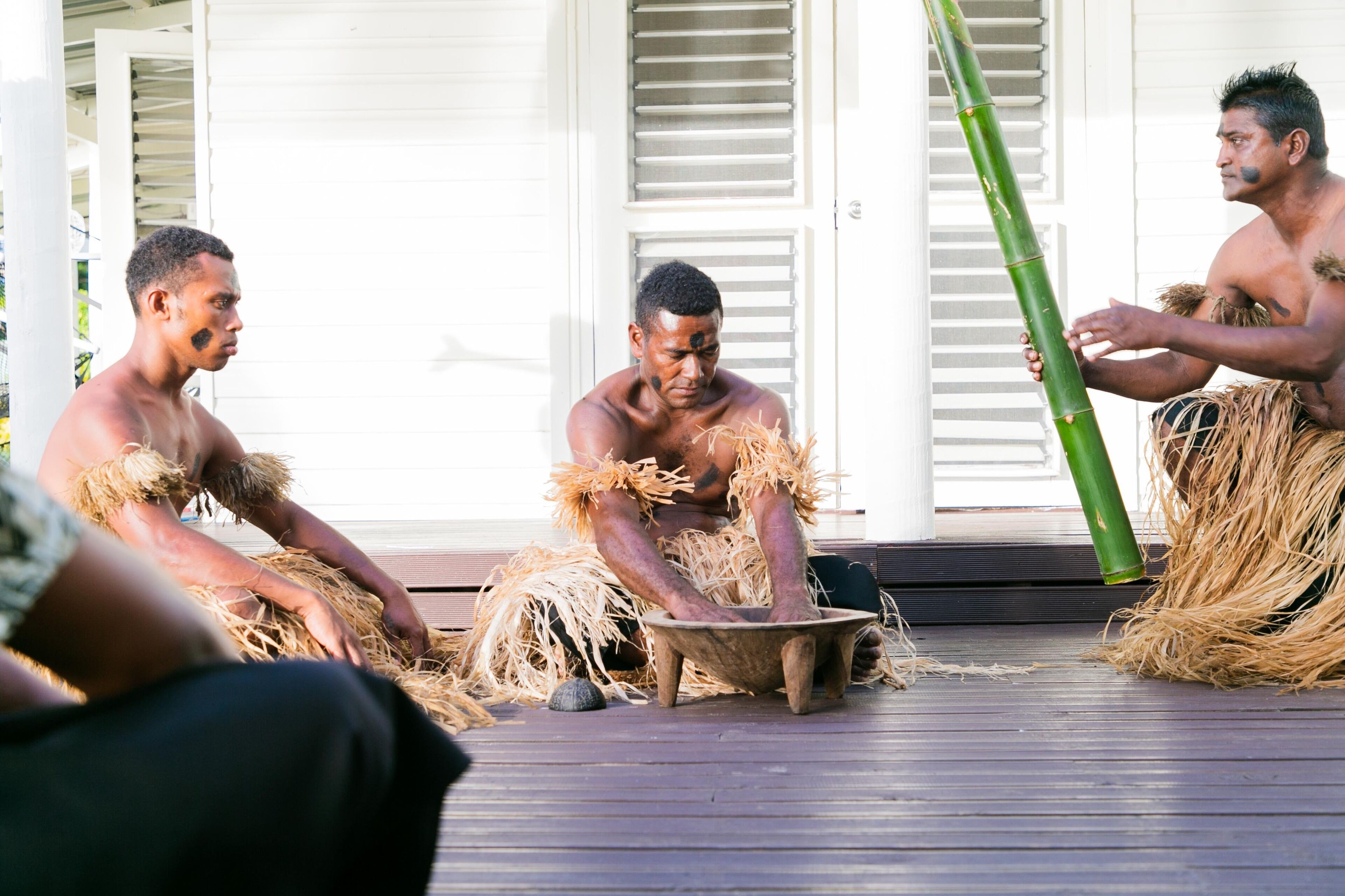 Three individuals in traditional attire sitting on a wooden deck.