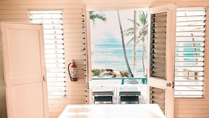 Une chambre avec vue sur une piscine et des palmiers, un ventilateur de plafond et une table agrémentée d’un vase décoratif.