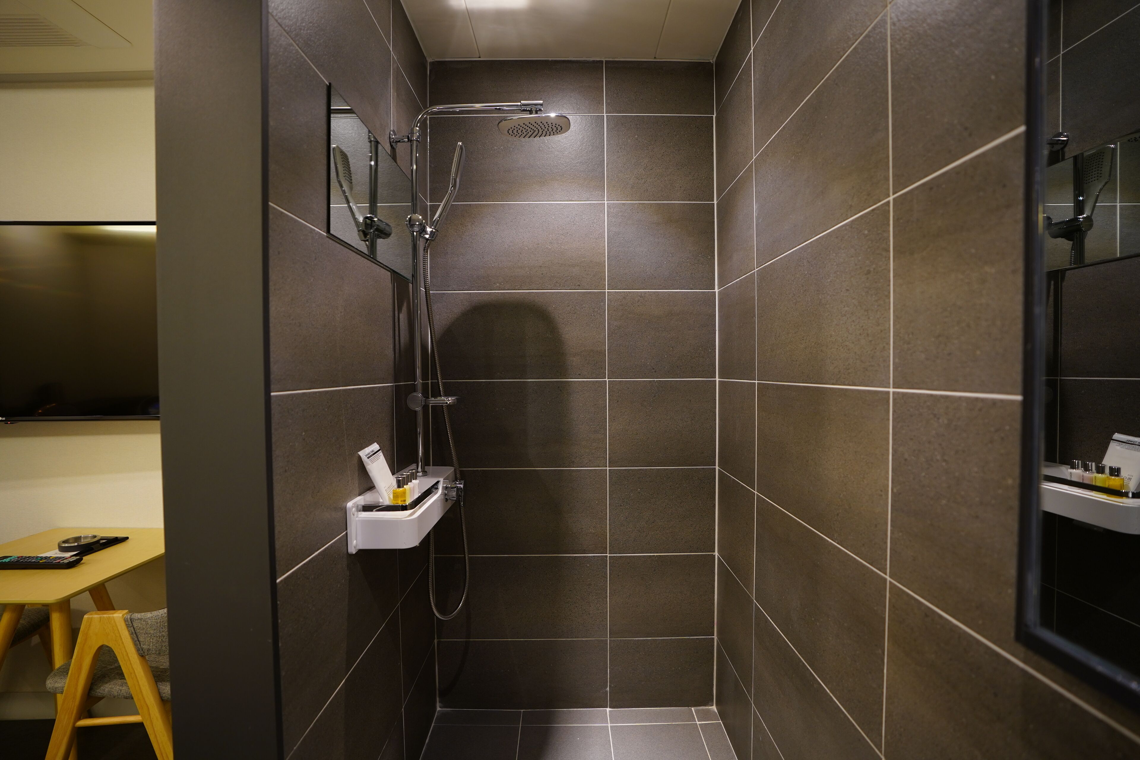 A small, modern shower area with a handheld showerhead and a wall-mounted faucet.