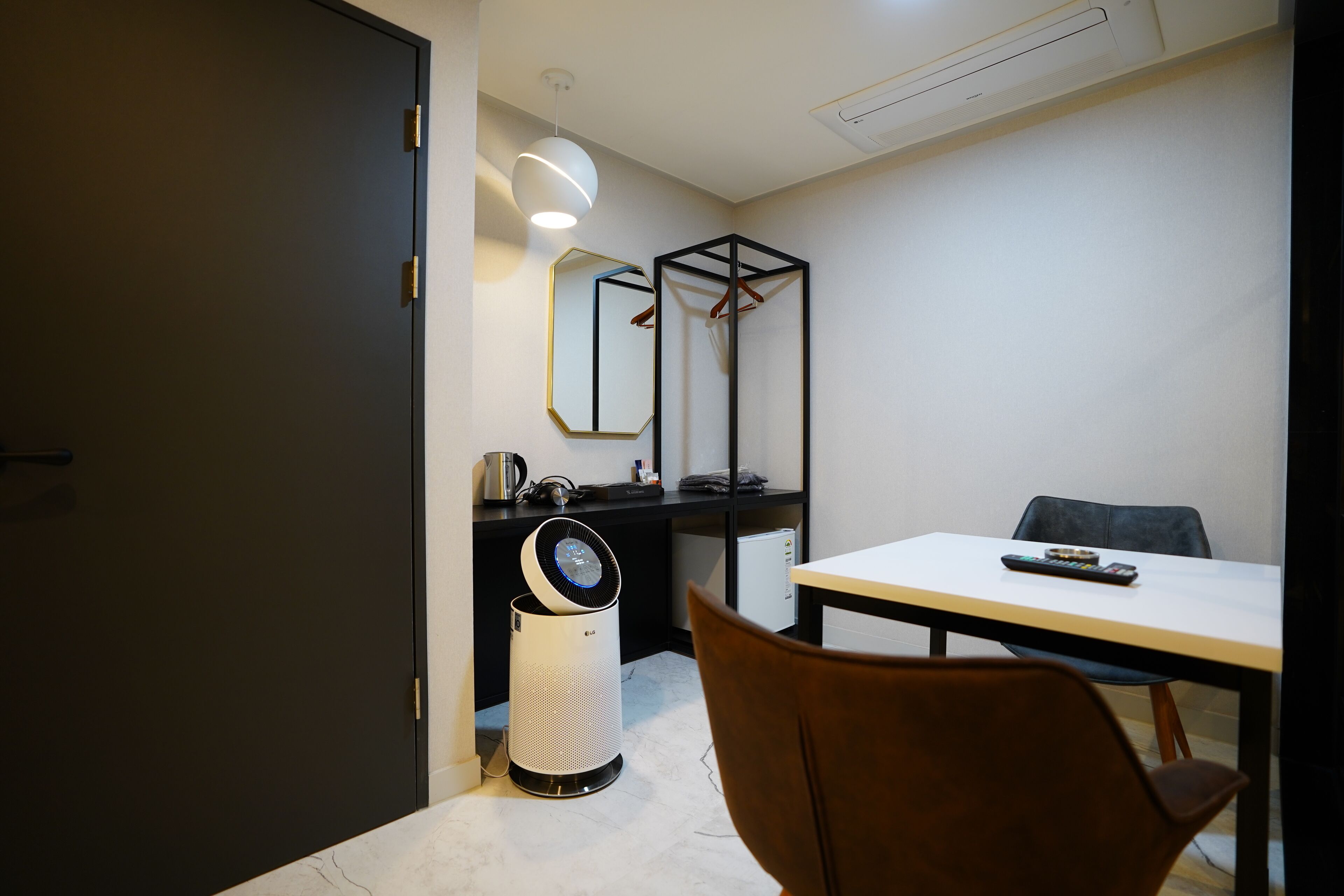 A compact room with a white table, a chair, a black wardrobe, a mirror, and a ceiling fan.