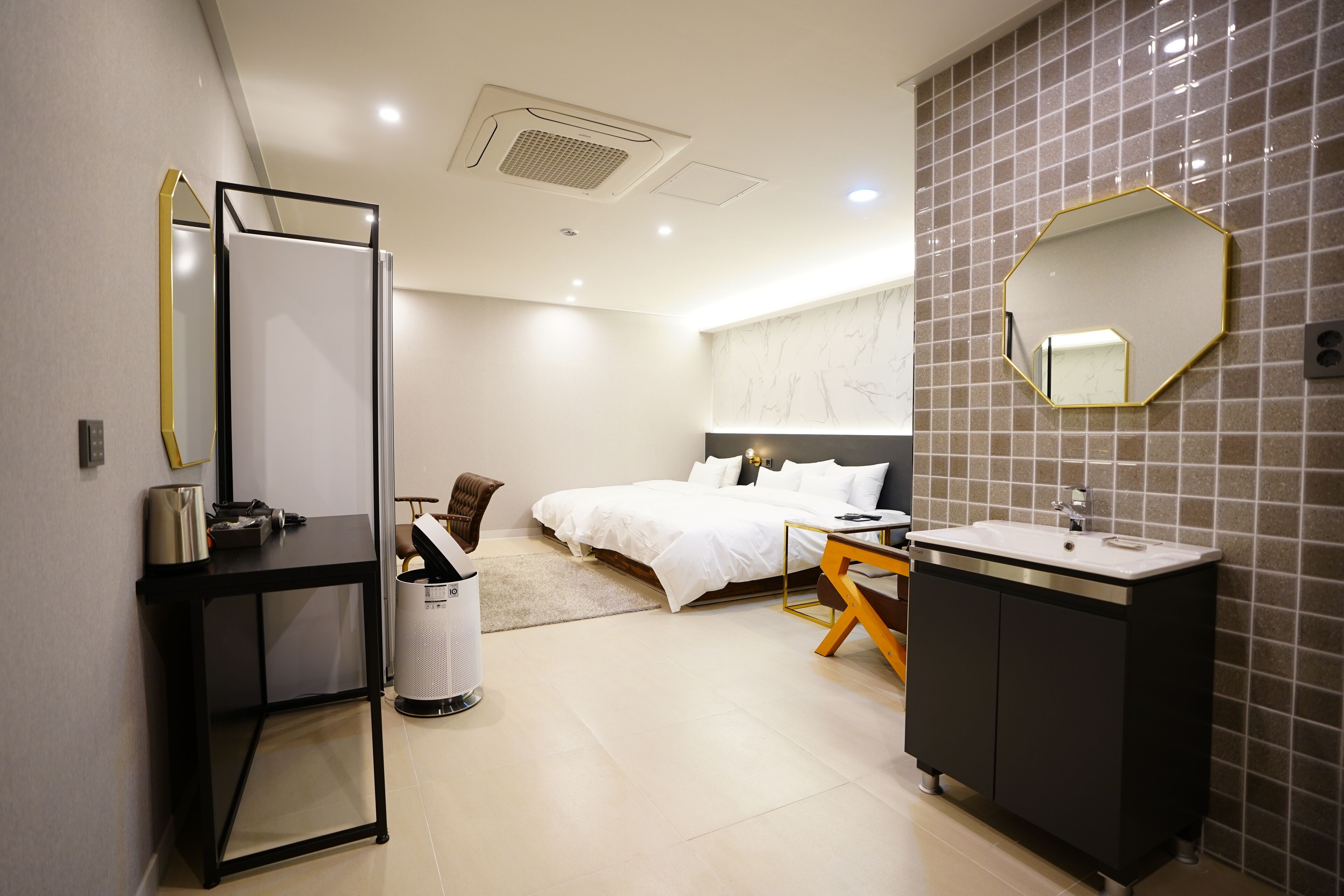 Moderni hotellihuone, jossa on sänky, työpöytä, peili, pesuallas ja roskakori.