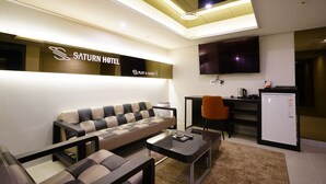 Ein modernes Hotelzimmer mit Sofa, Couchtisch, Fernseher, einer kleinen Küchenzeile und einem Kühlschrank.