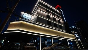 Ein Hotel mit moderner Fassade, beleuchteter Beschilderung und einem Parkplatz mit mehreren Autos.