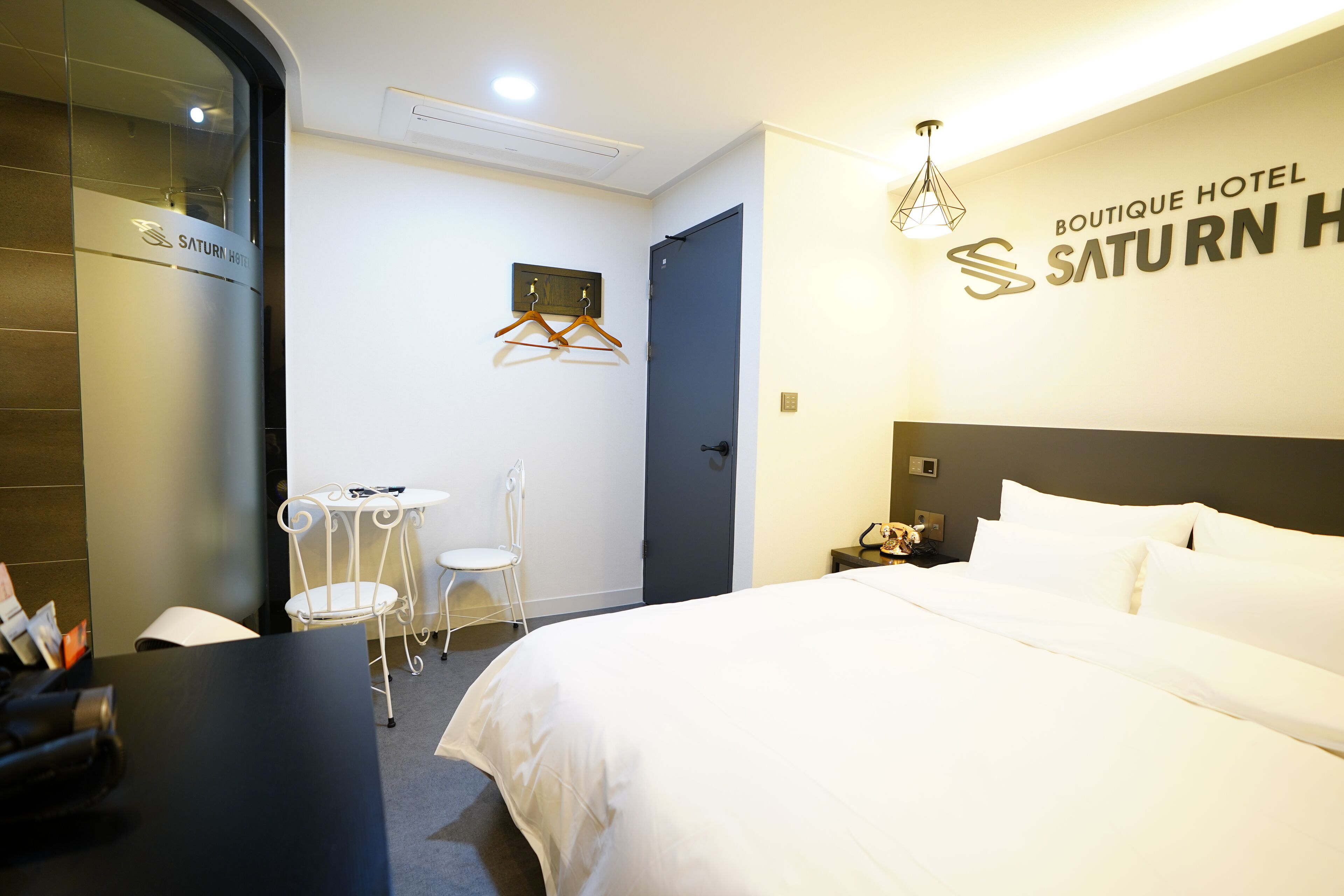 A hotel room with a bed, a desk, a chair, a coat rack, and a wall-mounted coat stand.