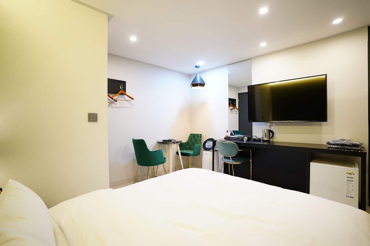 A hotel room with a bed, a desk with a flat-screen TV, a mini-fridge, and two chairs.