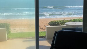 A room with a large window overlooking a beach and ocean. There is a chair with a cushion and a small table. - Direct Oceanfront 1/1 king first floor, oceanfront Patio, pool beach steps away. (Ormond Beach)