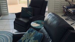 A room with a black leather sofa and armchair, a small round table, and a view of the beach through a sliding glass door. - Direct Oceanfront 1/1 king first floor, oceanfront Patio, pool beach steps away. (Ormond Beach)
