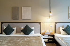 A hotel room with two beds, each with a headboard and pillows. There is a bedside table with a lamp and a small shelf with towels. - Jinyou Hotel (Chishang)