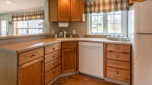 A kitchen with wooden cabinets, a dishwasher, and a window with curtains.