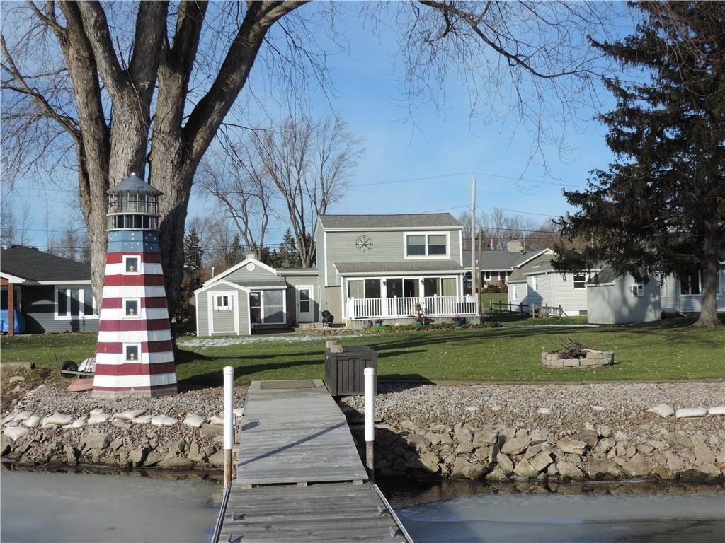 A waterfront property with a lighthouse, a dock, and a large house with a porch.