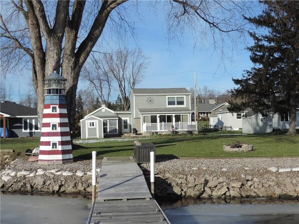 A waterfront property with a lighthouse, a dock, and a large house with a porch.