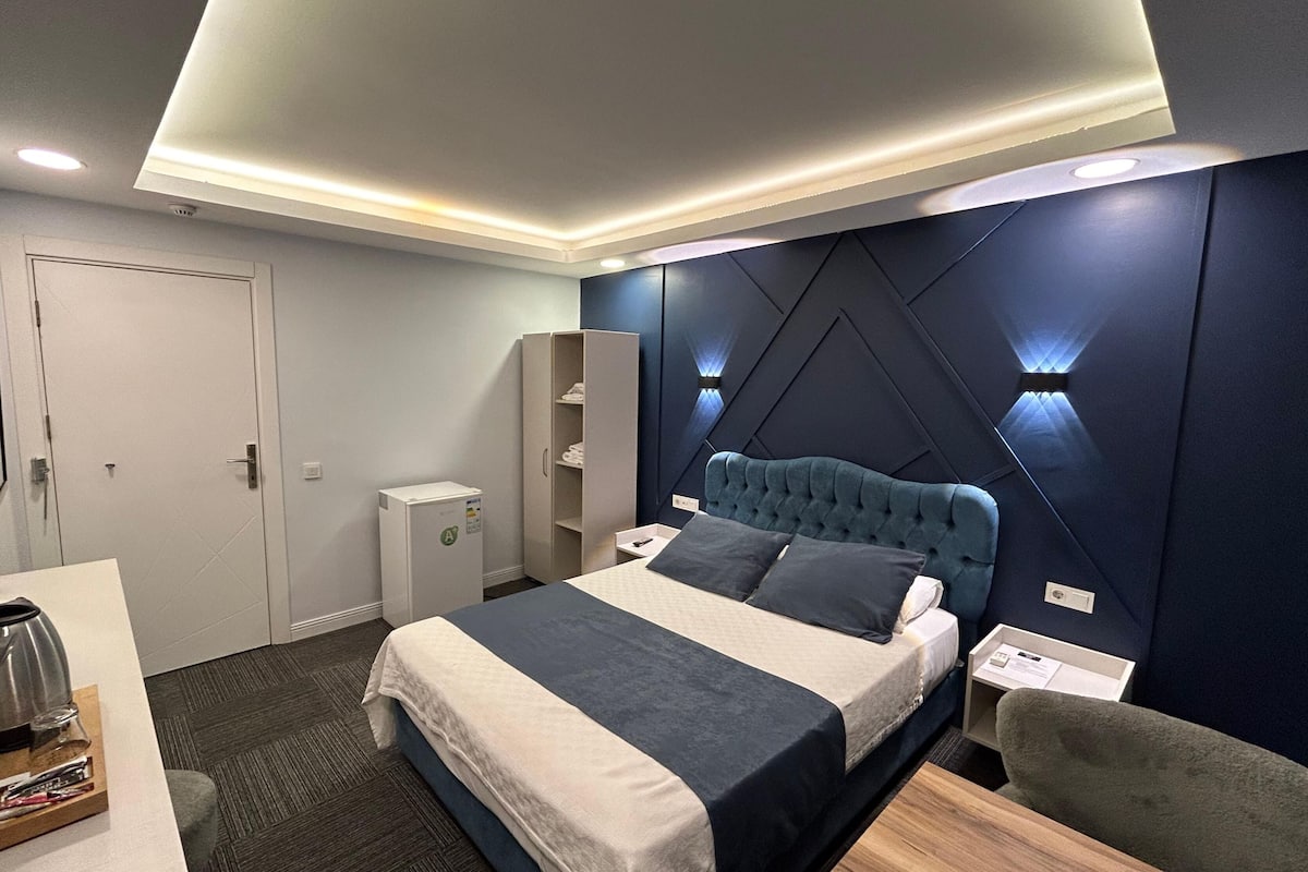 Moderni hotellihuone, jossa on suuri sänky, yöpöydät, vaatekaappi ja työpöytä sekä vedenkeitin.