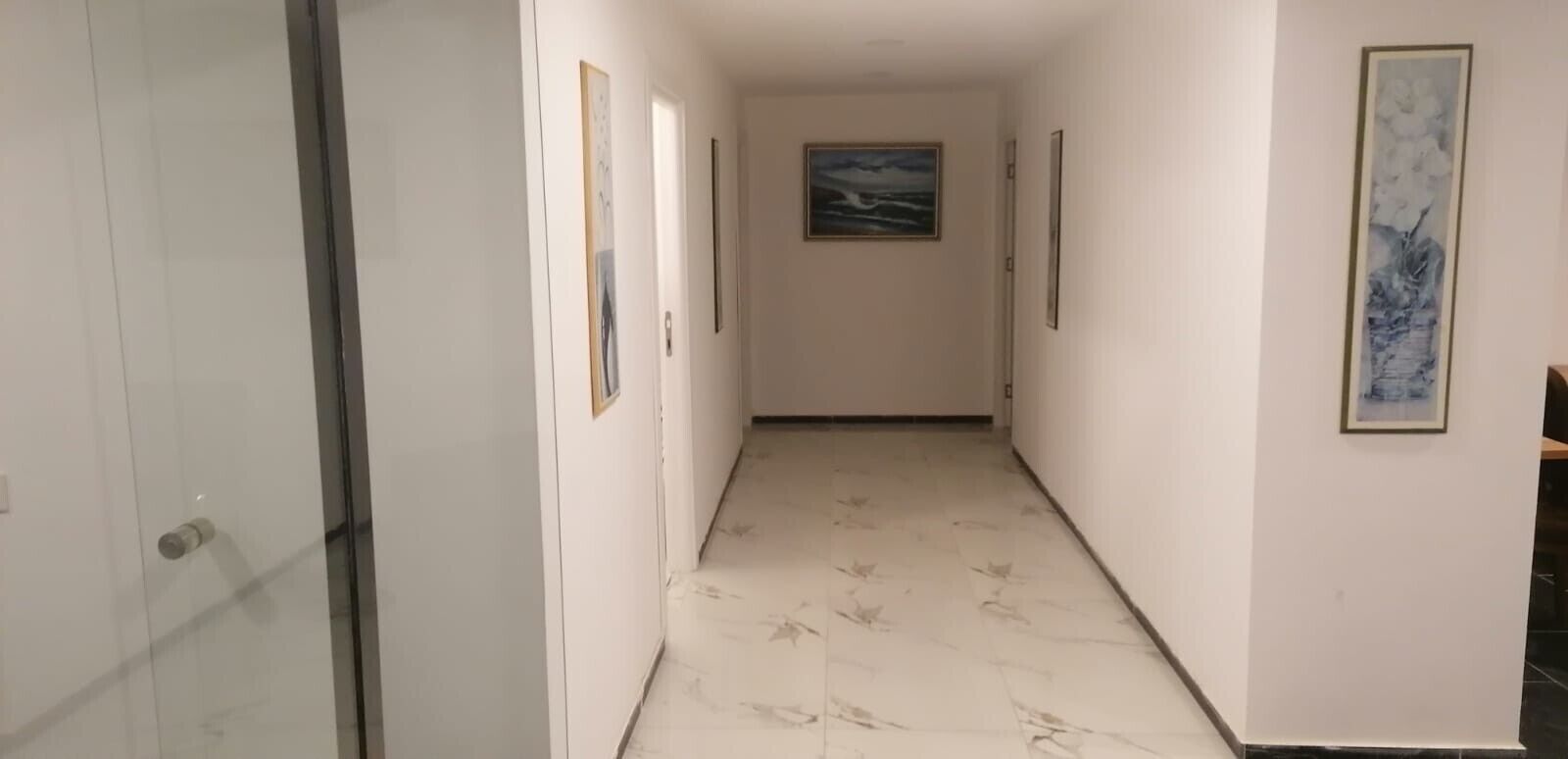 Un corridoio con pareti bianche, pavimento in marmo e opere d'arte incorniciate alle pareti.