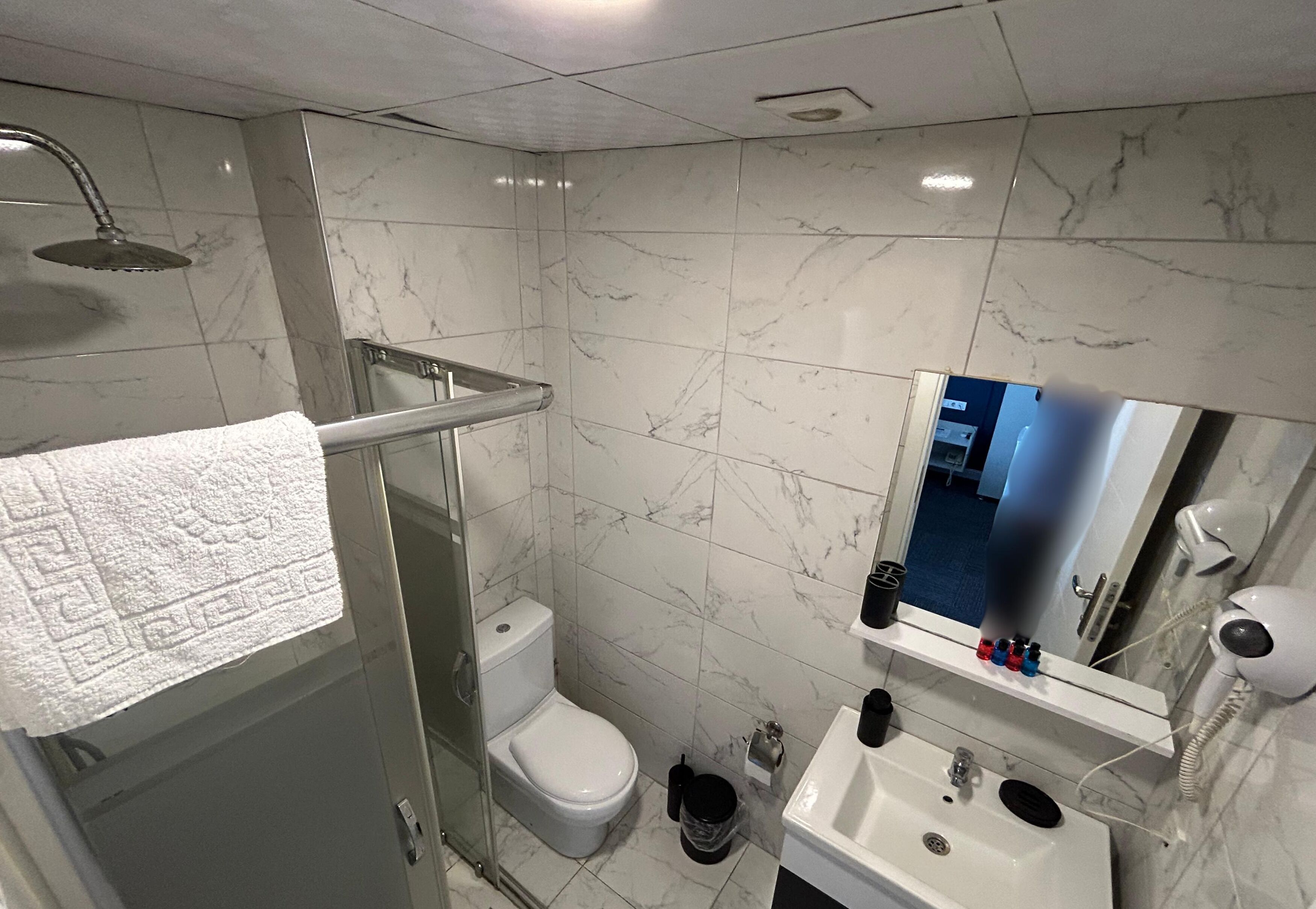 A bathroom with a glass shower enclosure, a toilet, a sink with a mirror, and a hairdryer on the wall.