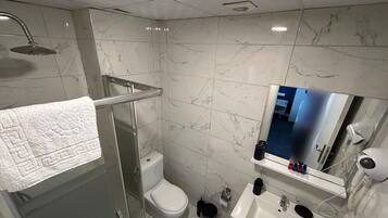 A bathroom with a glass shower enclosure, a toilet, a sink with a mirror, and a hairdryer on the wall.