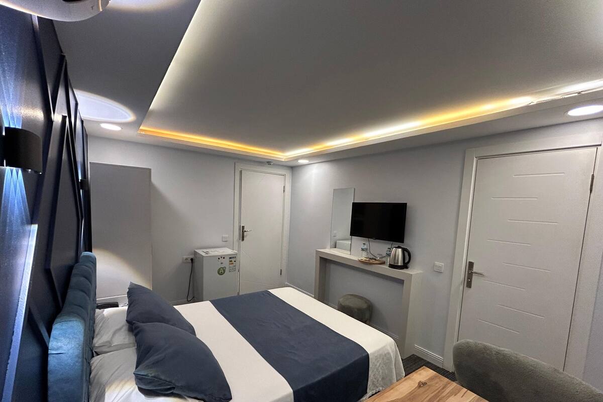 Moderni hotellihuone, jossa on sänky, pieni työpöytä, televisio ja ovi.