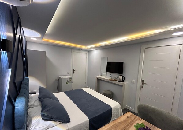Moderni hotellihuone, jossa on sänky, pieni työpöytä, televisio ja ovi.