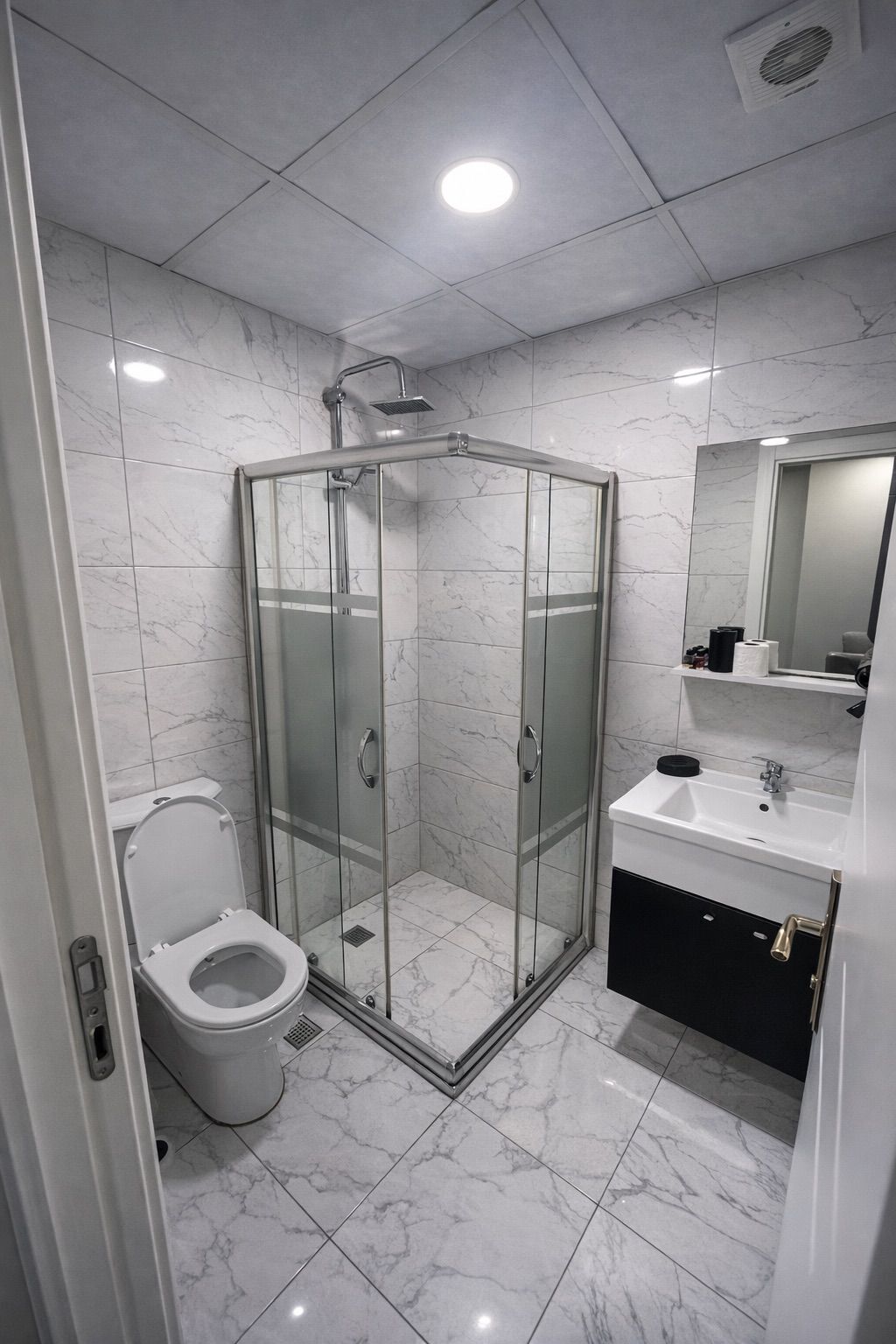 Une salle de bain moderne avec une douche à parois de verre, des toilettes et un lavabo surmonté d’un miroir.