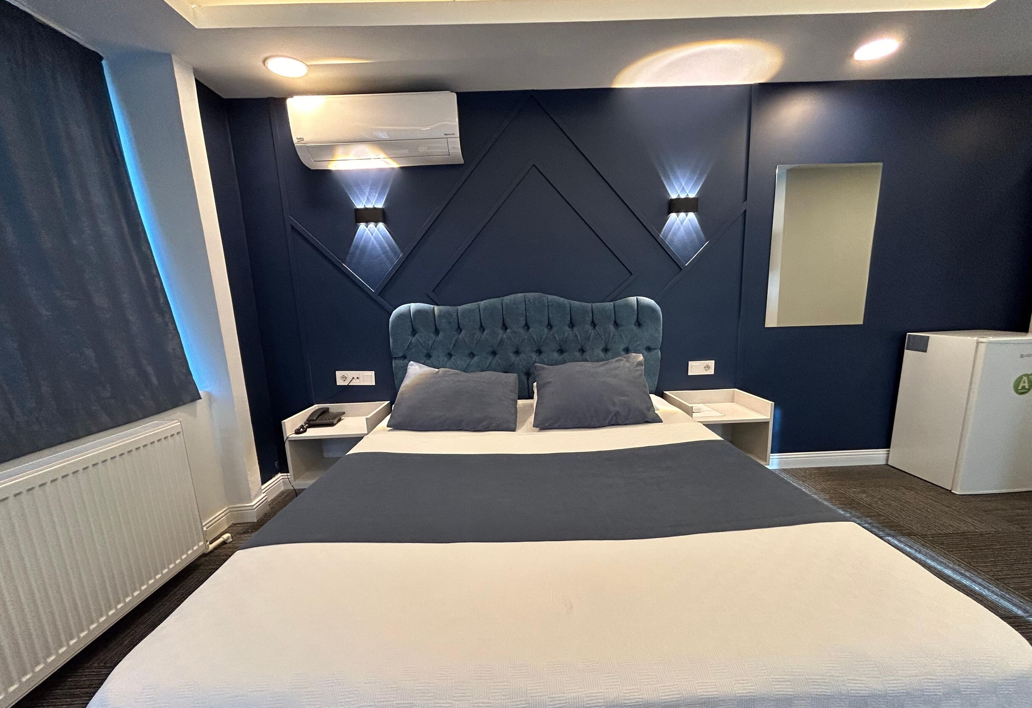 A modern hotel room with a large bed, two bedside tables, a built-in wardrobe, and a wall-mounted air conditioner.