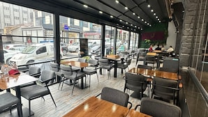 An indoor dining area with tables and chairs, large windows, and a view of the street outside. - Kavacık Asia Hotel (Beykoz)