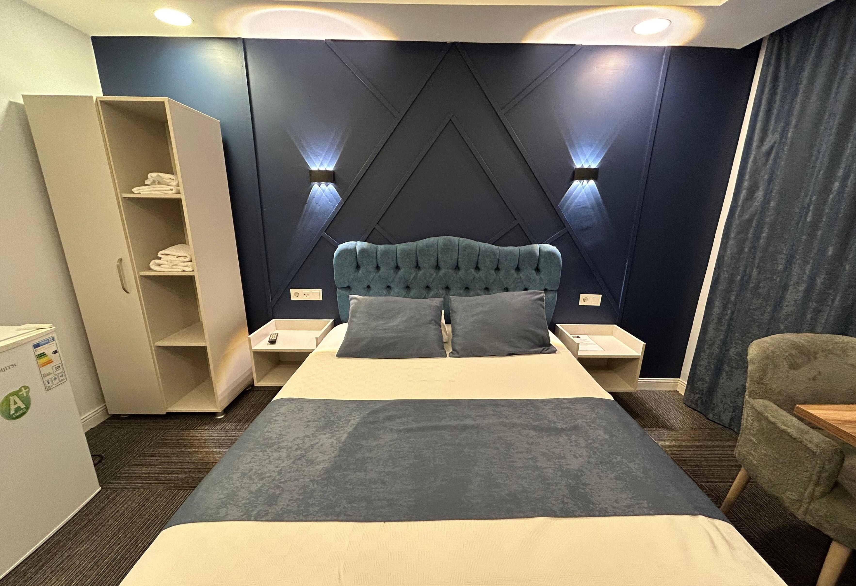 Una habitación de hotel con una cama grande, un armario, dos mesitas de noche y una silla.