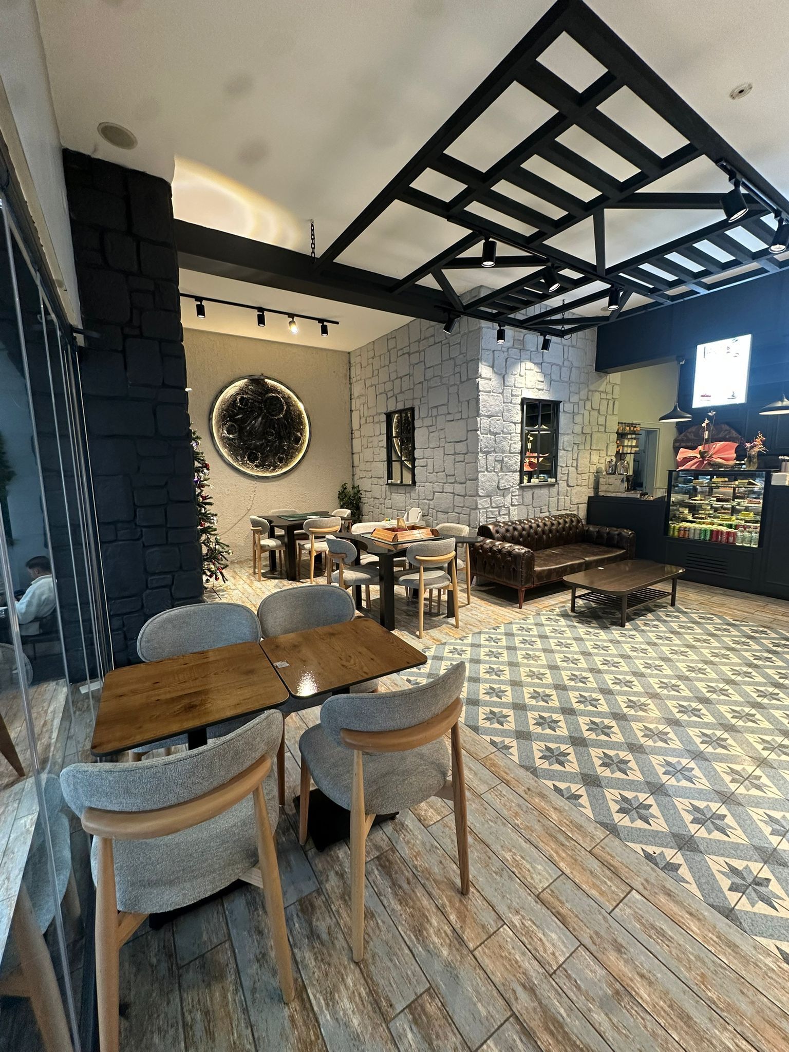 Ein modernes Café mit Holztisch und -stühlen, Steinwänden und einem gemusterten Boden.
