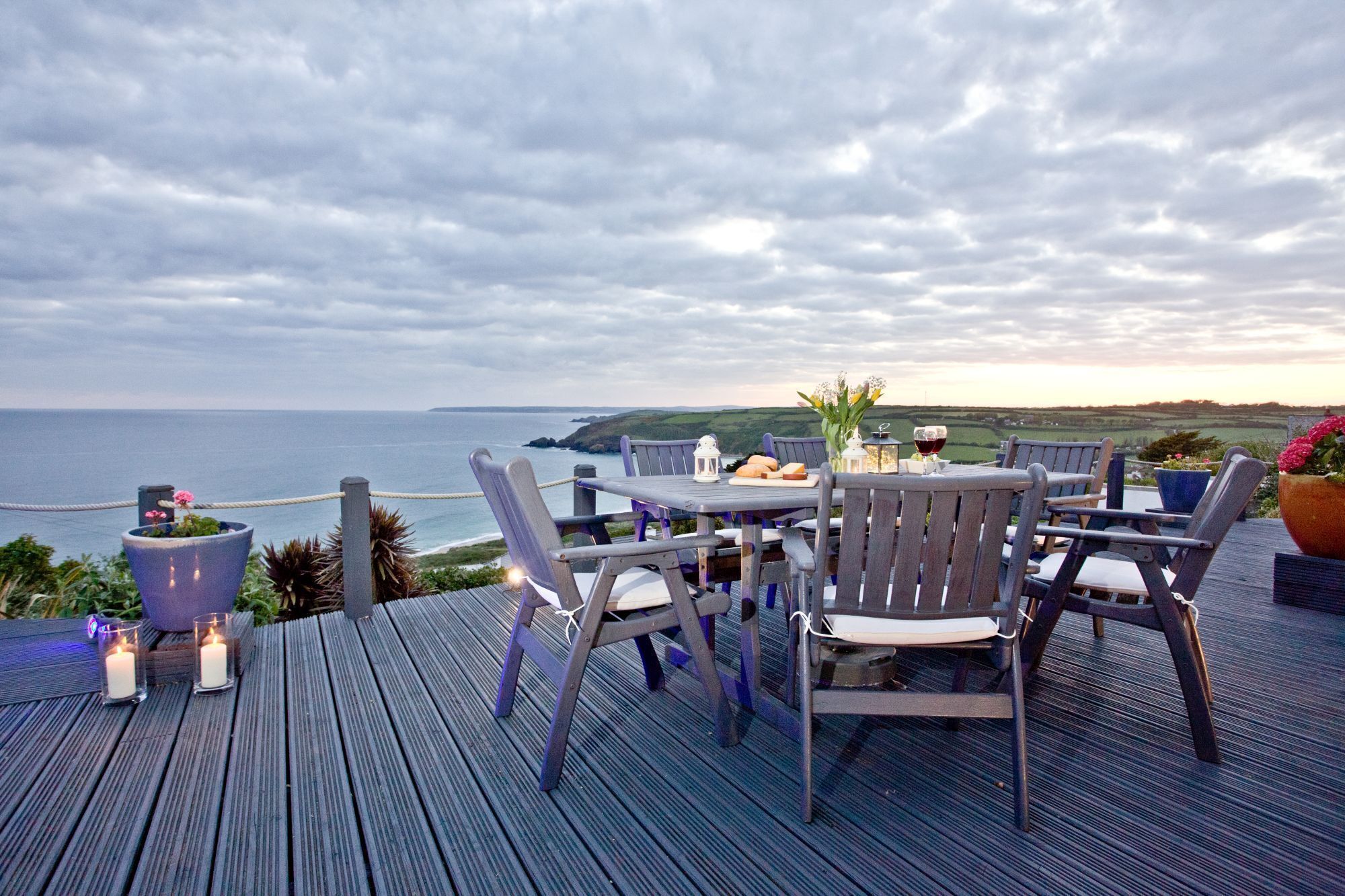 Une terrasse en bois avec une table et des chaises, offrant une vue sur un paysage côtier.