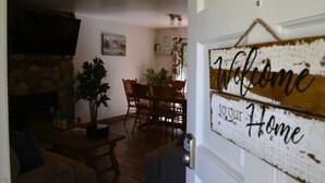A cozy living room with a fireplace, a dining area with wooden furniture, and a 'Welcome to our Home' sign.
