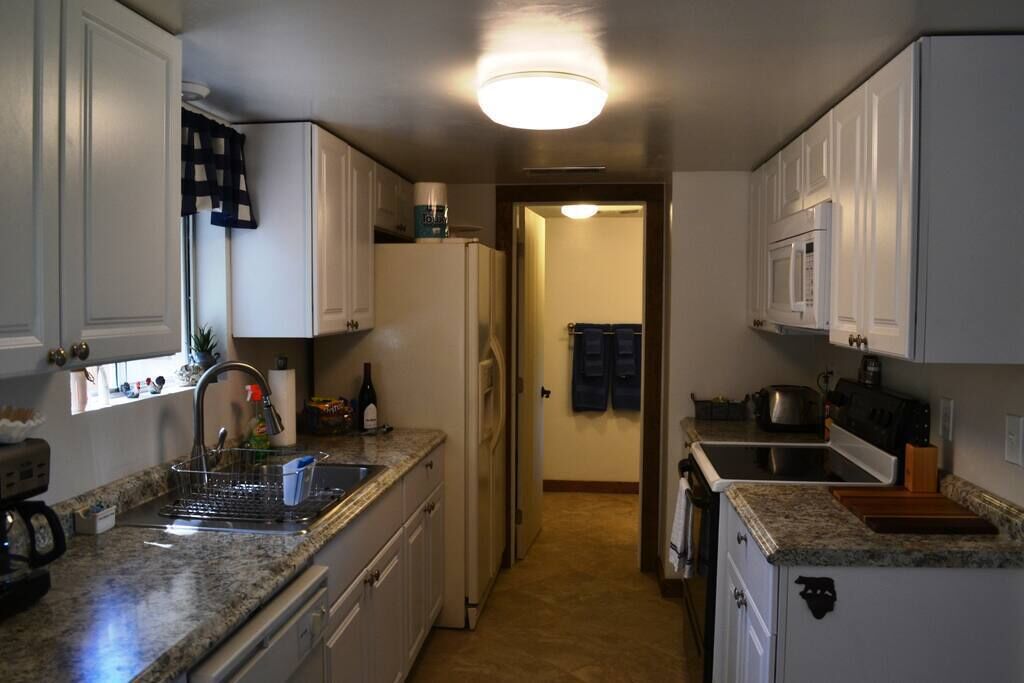 A compact kitchen with white cabinets, a granite countertop, and a central island.