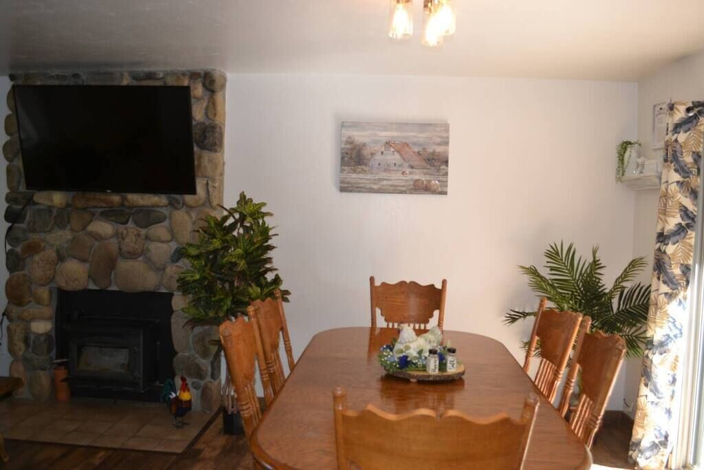 Un área de comedor con chimenea de piedra, un televisor de pantalla plana montado encima y un cuadro en la pared.
