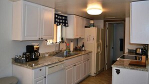 A compact kitchen with white cabinets, a granite countertop, a built-in dishwasher, and a refrigerator.