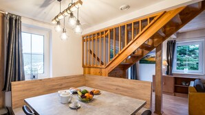 A modern kitchen with a wooden table, chairs, and a fruit bowl. A staircase with wooden railings leads to another level. - Holiday Hill 65 by Interhome (Cerny Dul/Cista)