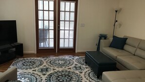 A living room with a sofa, ottoman, and a TV on a stand. - Wakulla River Retreat- Manatee Cottage  (Crawfordville)