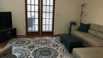 Un salon avec un canapé, un pouf et un téléviseur posé sur un meuble.