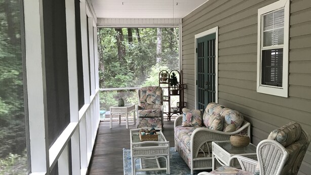 A covered porch with wicker furniture, a ceiling fan, and a view of the forest. - Wakulla River Retreat- Manatee Cottage  (Crawfordville)