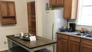 A kitchen with wooden cabinets, a white refrigerator, a coffee maker, and a rug. - Wakulla River Retreat- Manatee Cottage  (Crawfordville)