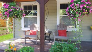 En inglasad veranda med två Adirondack-stolar, ett litet bord och hängande blomkorgar.